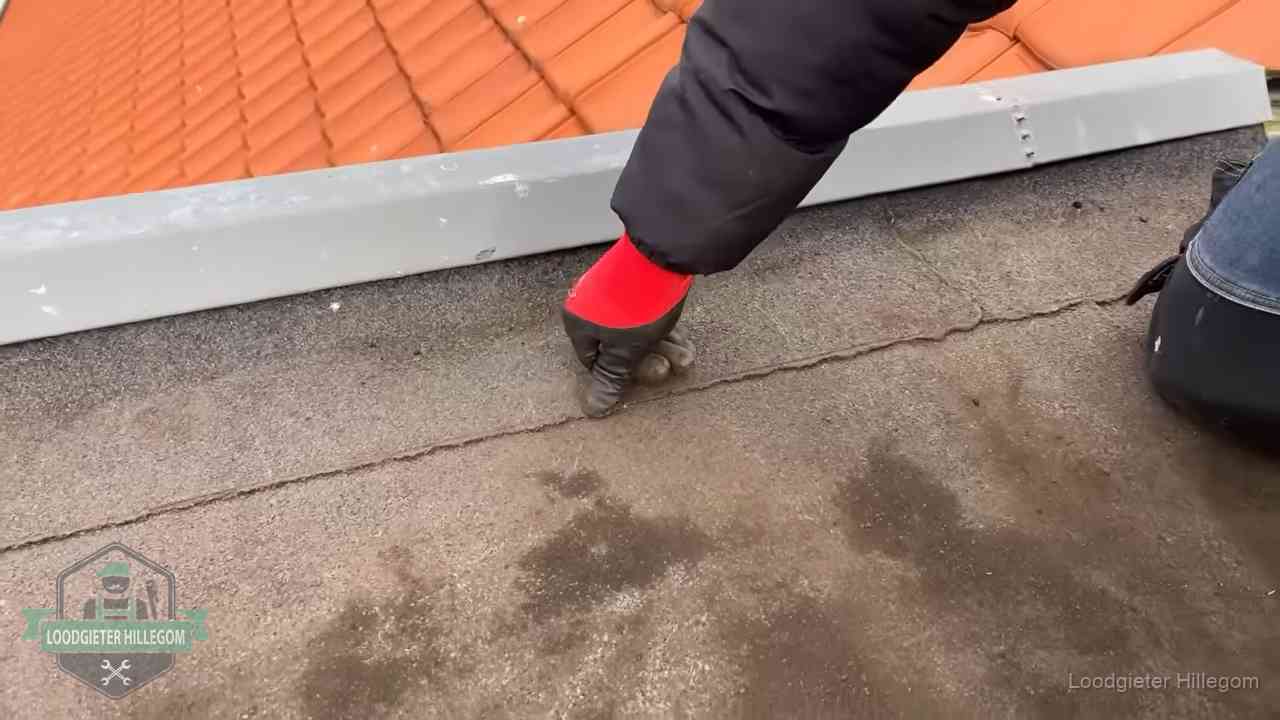 Vakman wijst een naad met vochtplekken aan op een bitumen plat dak in Hillegom