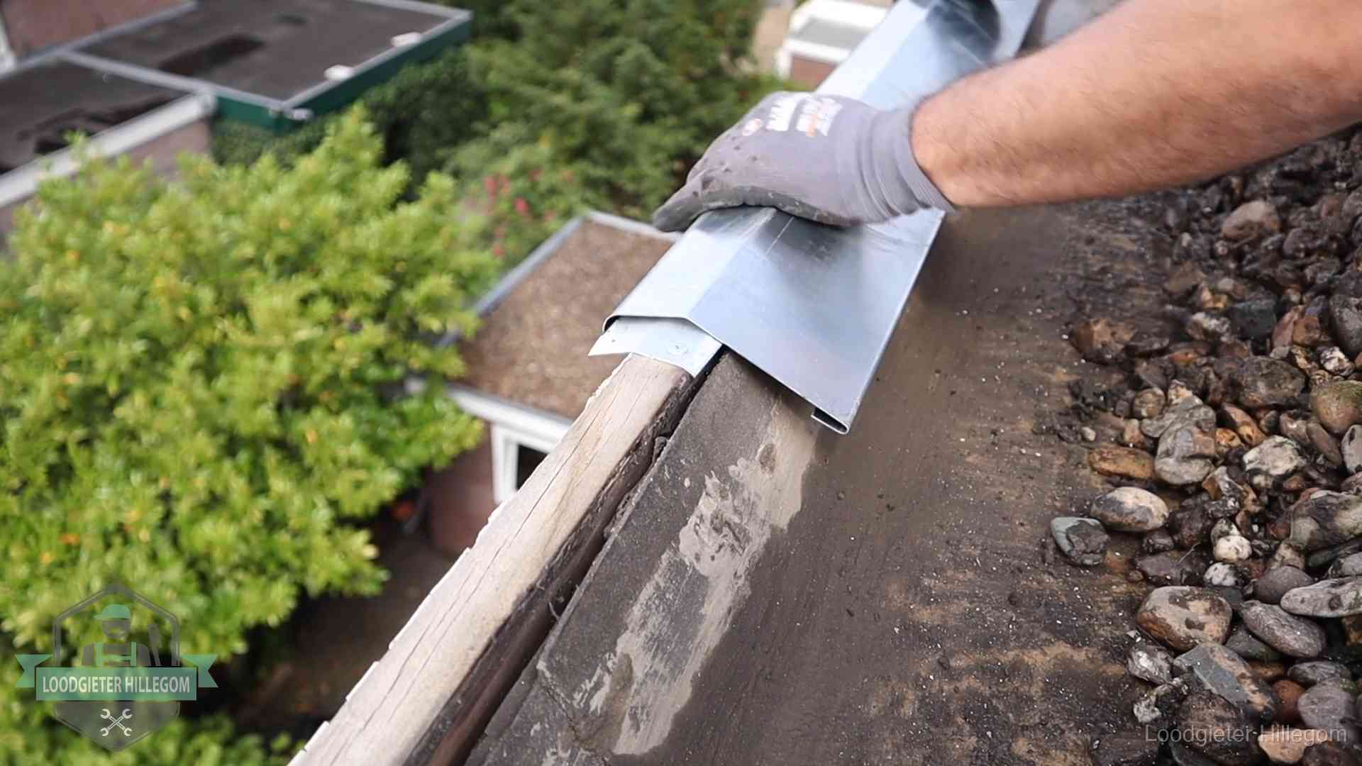 Dakdekker plaatst een zinken deklijst op een dakrand met uitzicht over een woonwijk in Hillegom