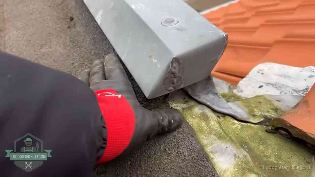 Controle van een zinken hemelwaterafvoer met loodslab bij dakpannen in Hillegom