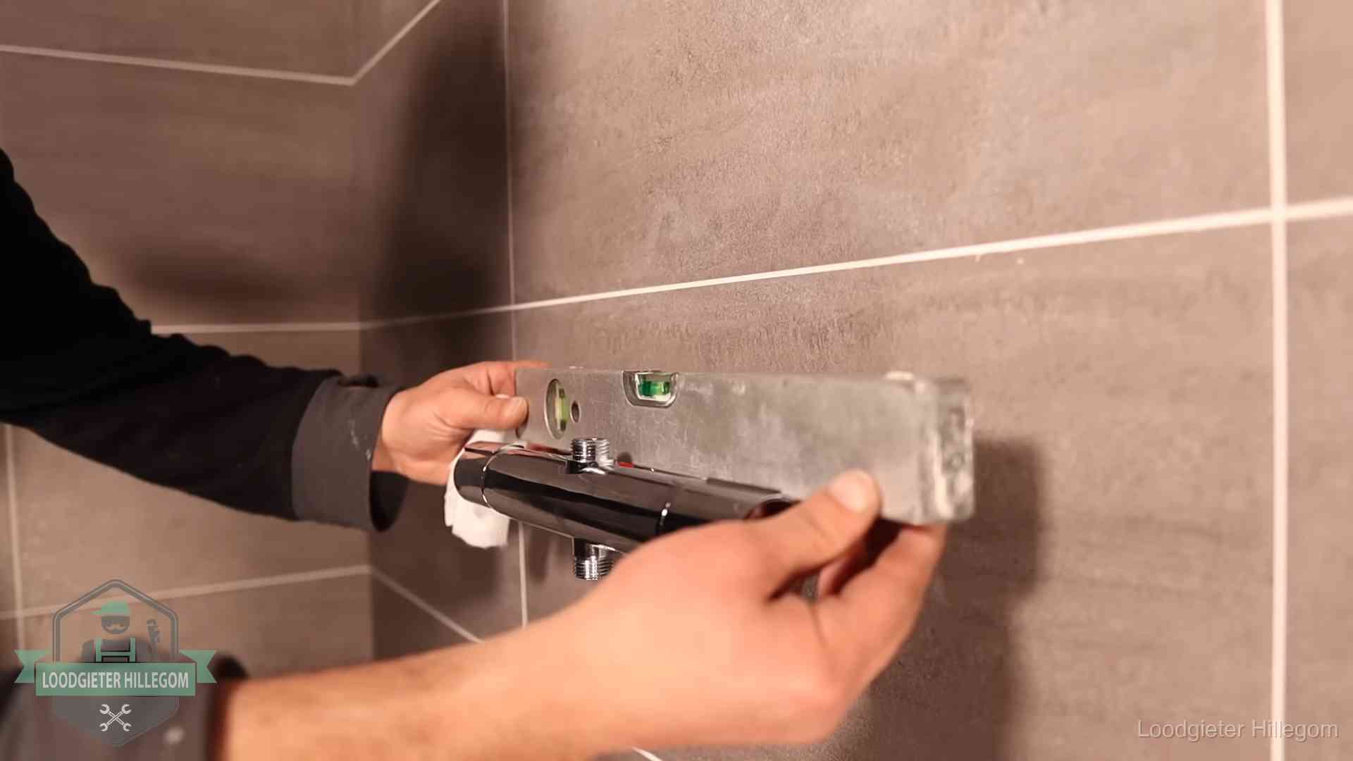 Loodgieter lijnt een douchekraan uit met een waterpas in een woning in Hillegom