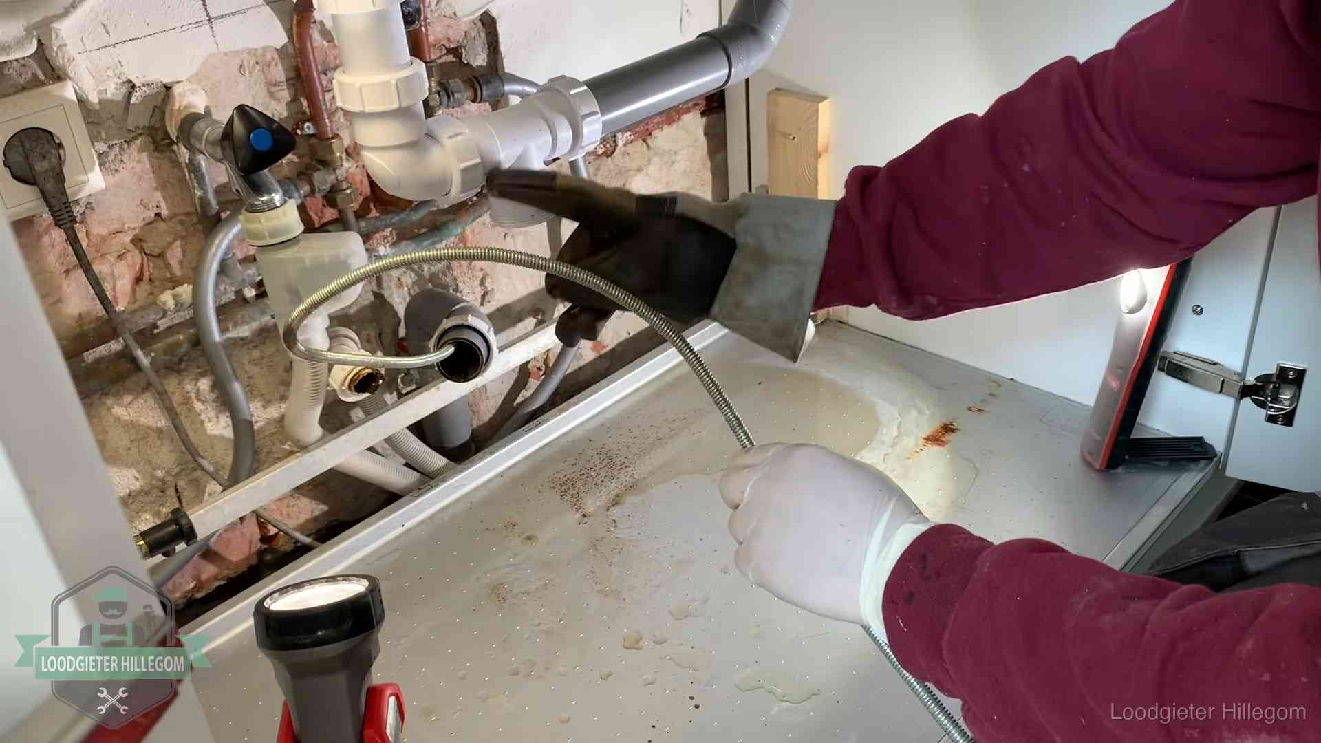 Ontstoppingsveer gaat in een geopende sifonaansluiting onder het aanrecht in Hillegom