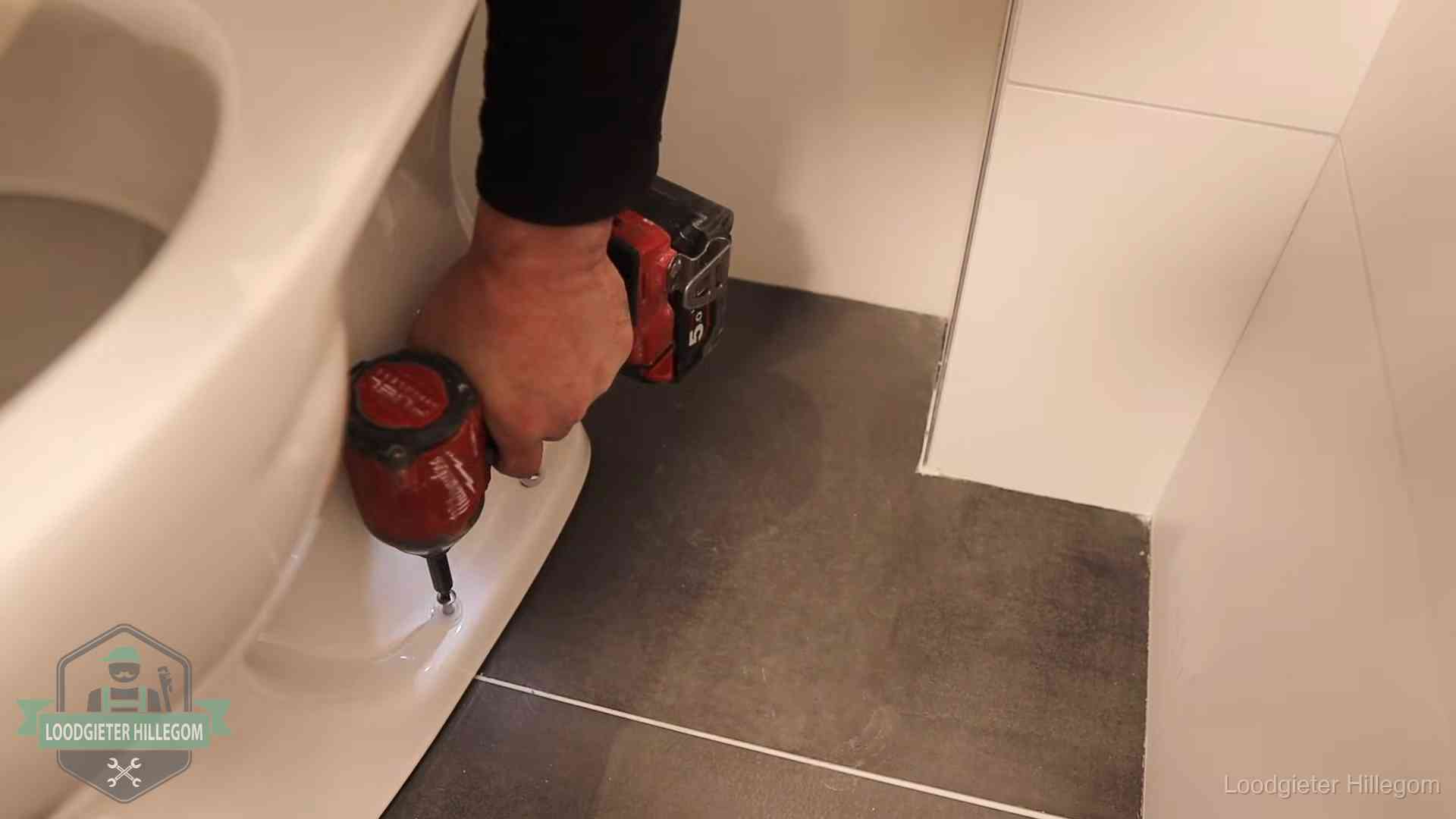 Loodgieter zet de voet van een wc-pot vast op de tegelvloer in Hillegom